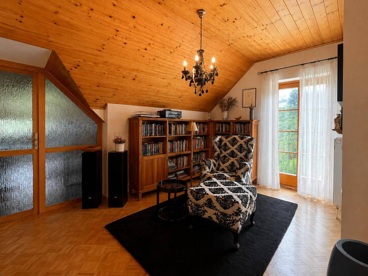 Heller Wohnbereich im Dachgeschoss mit Holzdecke, Lesesessel und Zugang zum Balkon.