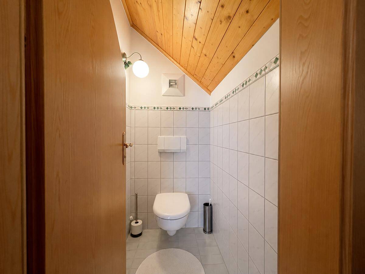 Kleines Gäste-WC im Dachgeschoss mit weißen Fliesen und Holzdecke.