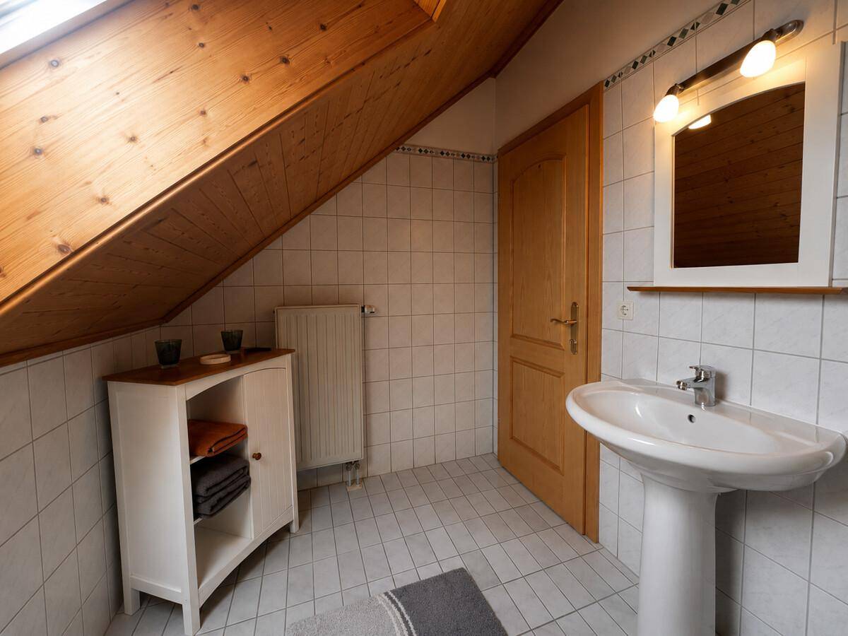 Badezimmer im Dachgeschoss mit Fliesenboden, Waschbecken und schräger Holzwand.