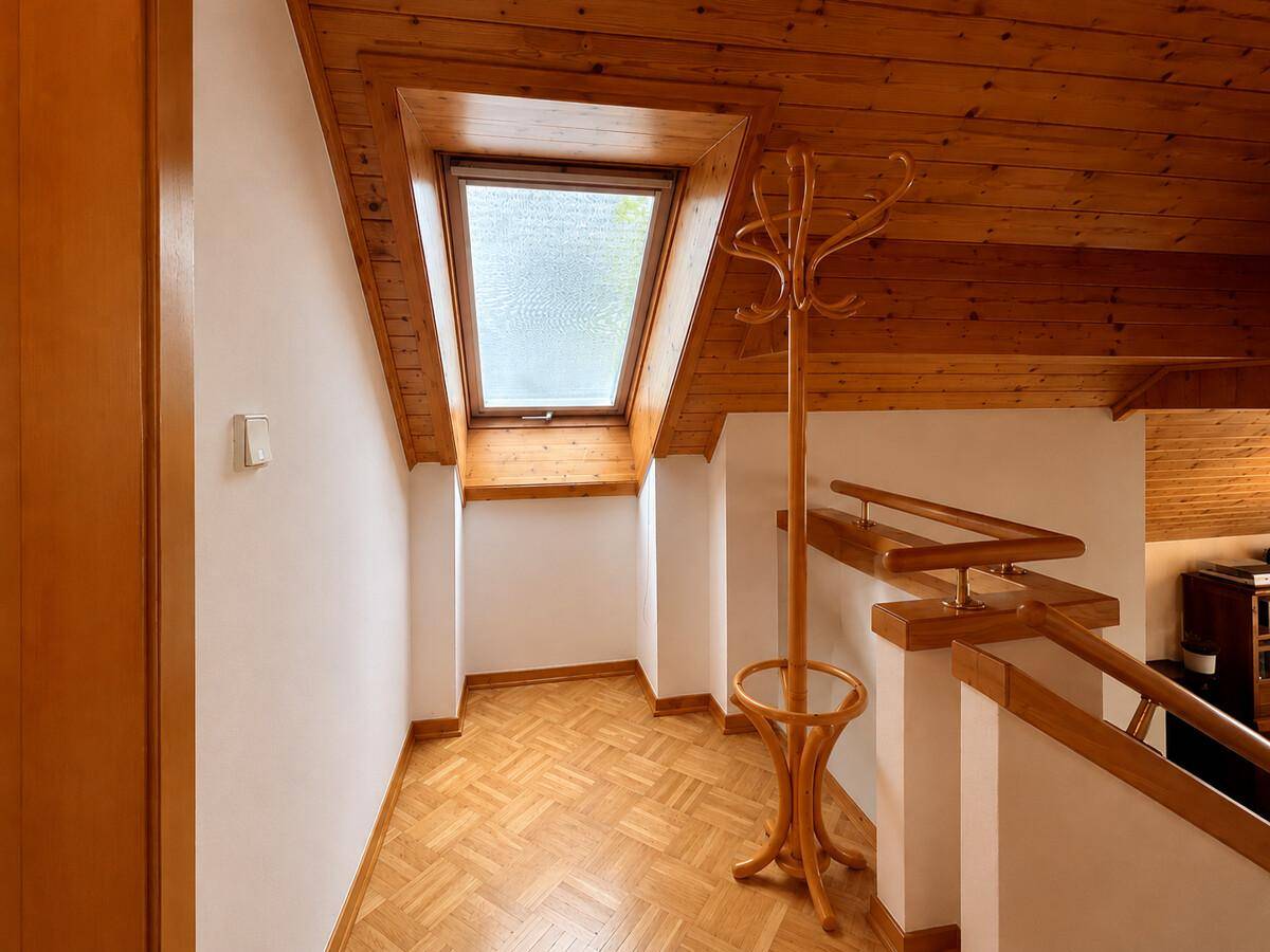 Heller Flurbereich im Dachgeschoss mit Holzgeländer, Dachfenster und Holztäfelung.