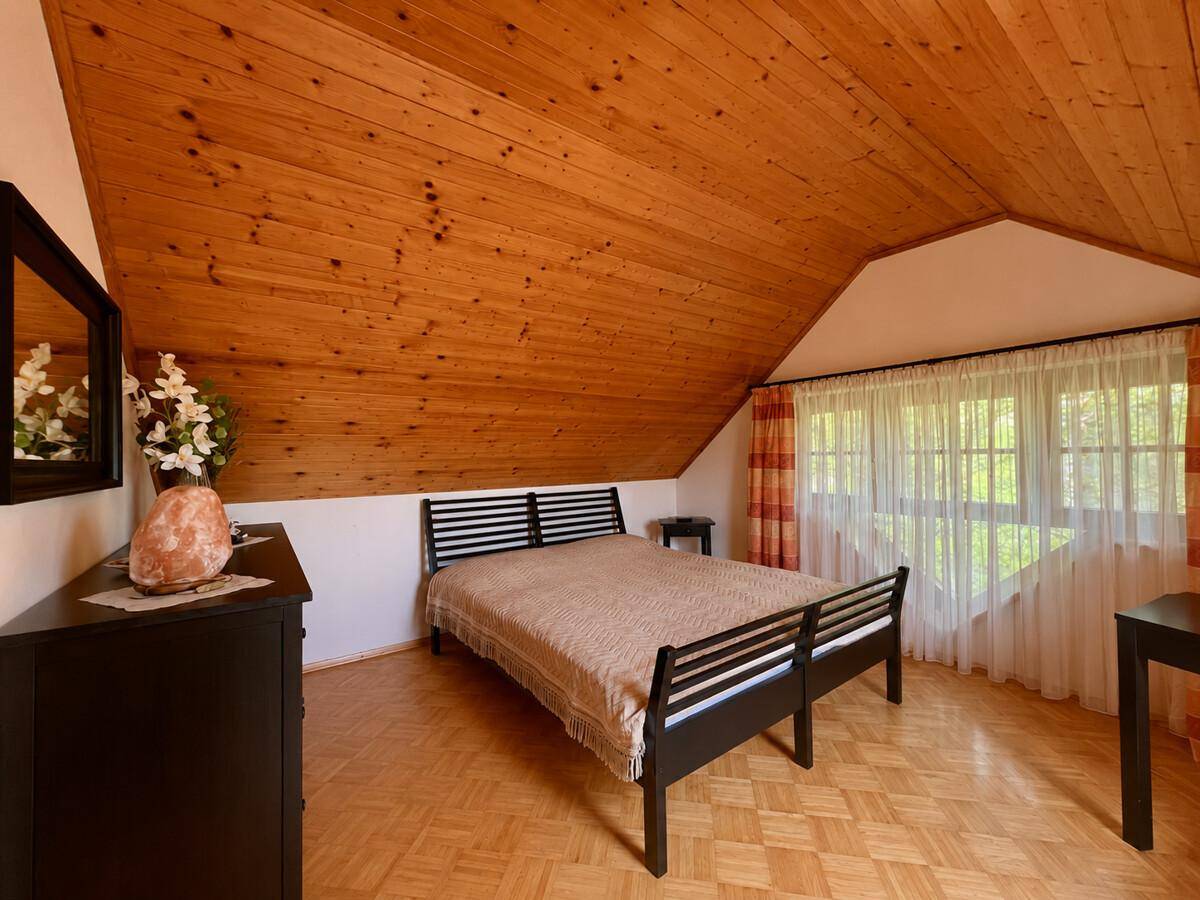 Gemütliches Schlafzimmer im Dachgeschoss mit Holzbalkendecke und Parkettboden.