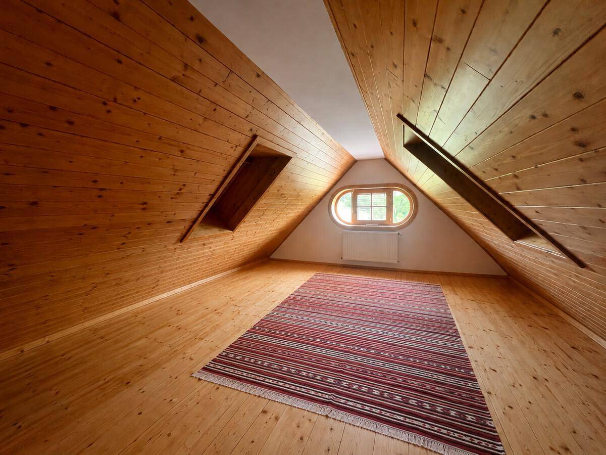 Heller Dachbodenraum mit Holztäfelung, schrägen Wänden und einem ovalen Fenster.