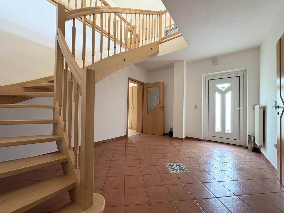Eingangsbereich mit Terrakotta-Fliesenboden und einer eleganten Holzwendeltreppe zum Obergeschoss.