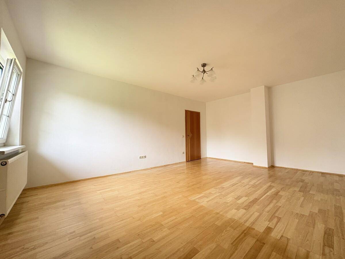 Geräumiges Schlafzimmer mit hellem Parkettboden, weißen Wänden und großem Fenster.