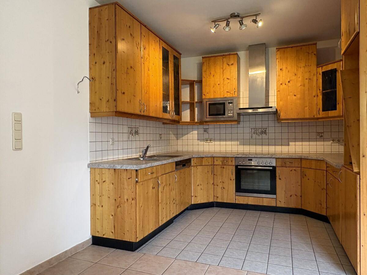 Traditionelle Einbauküche mit Holzschränken, Fliesenboden und integrierten Geräten.