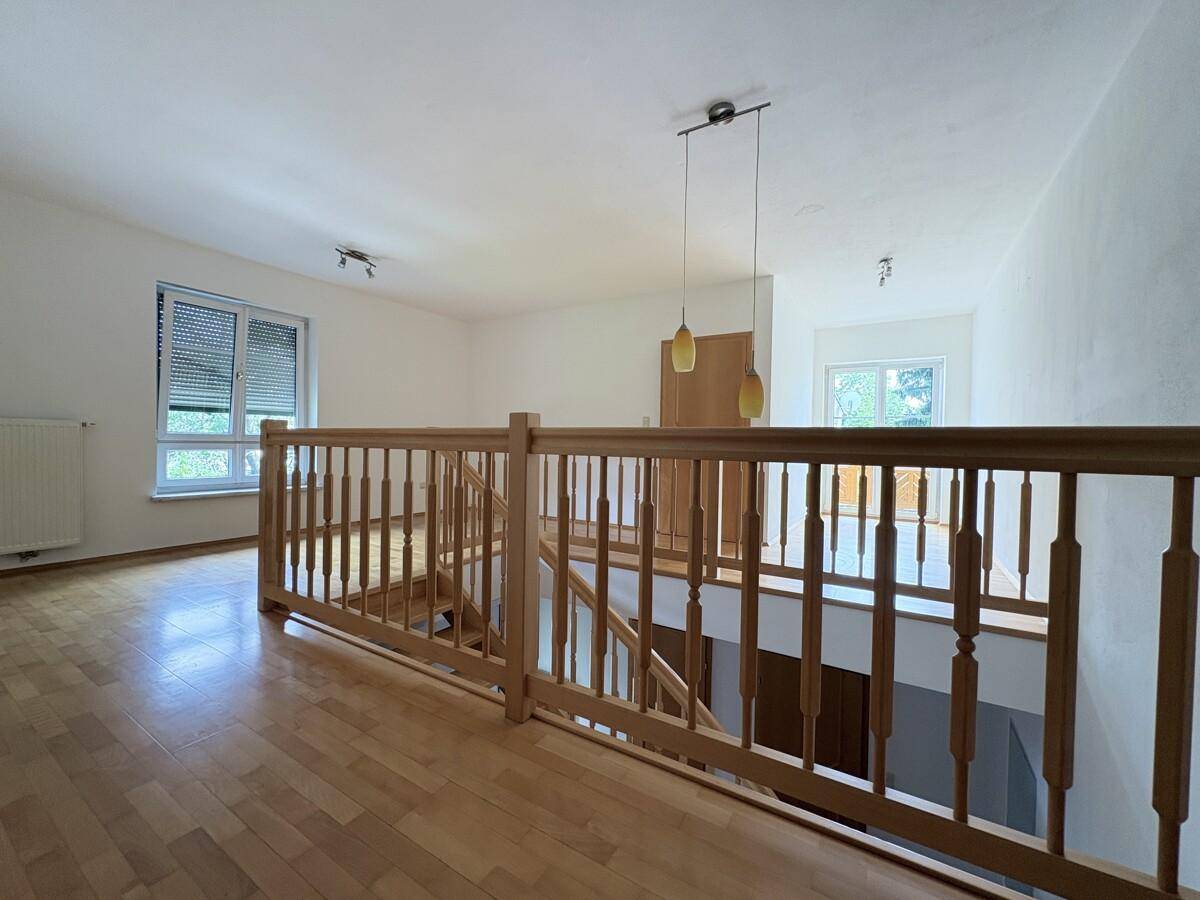 Heller Flur im Obergeschoss mit Holzgeländer, Parkettboden und Blick ins Grüne.