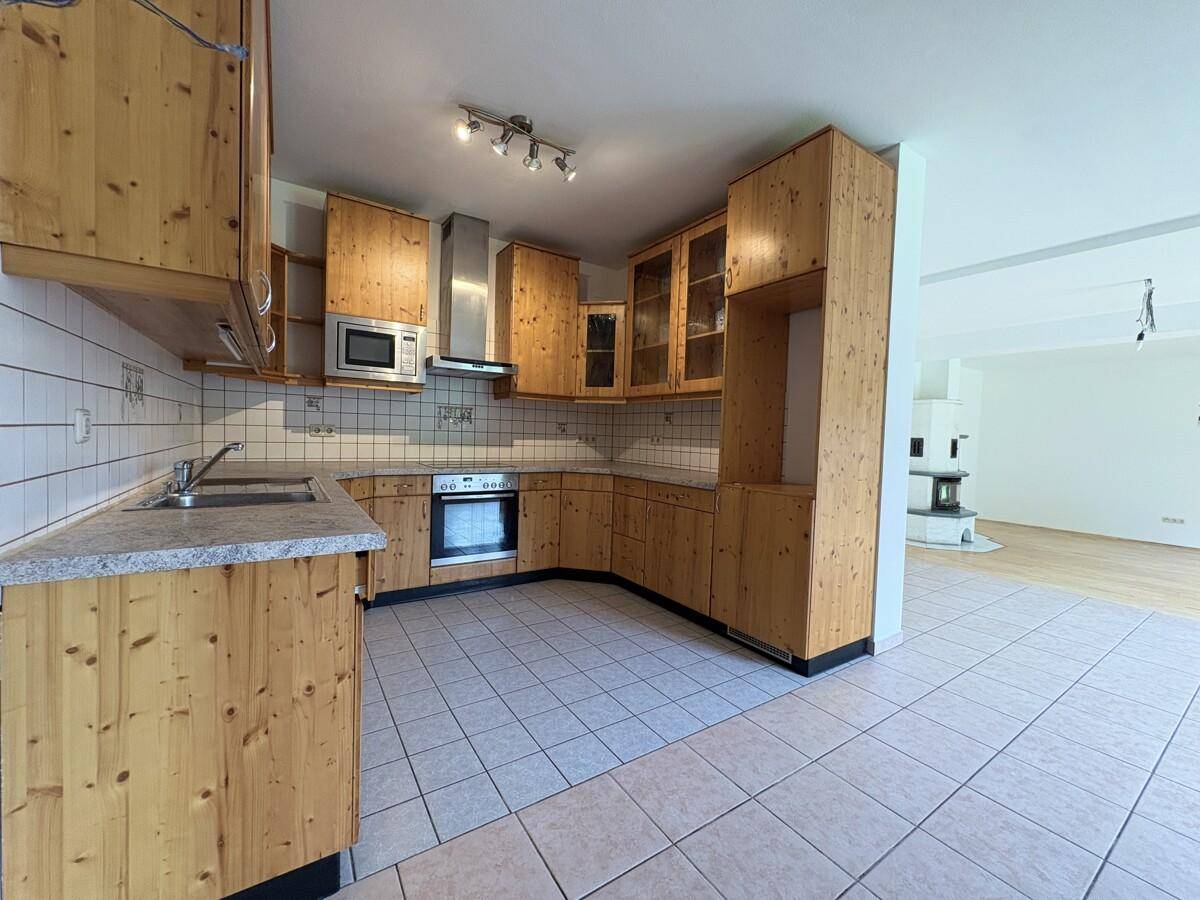 Gemütliche Küche mit Holzfronten, Fliesenboden und offenem Übergang zum Wohnbereich.