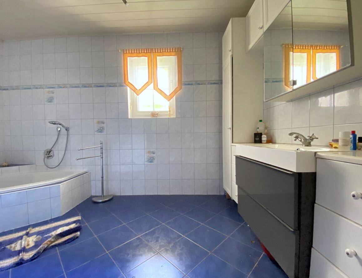 Badezimmer mit blauen Bodenfliesen, weißen Wandfliesen, Badewanne und Fenster.