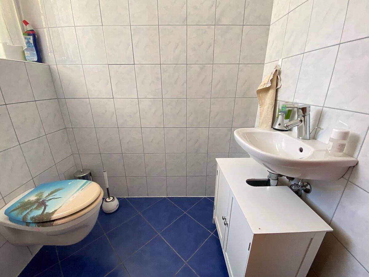 Kleines Gäste-WC mit blauen Bodenfliesen, weißen Wandfliesen und Waschbecken.