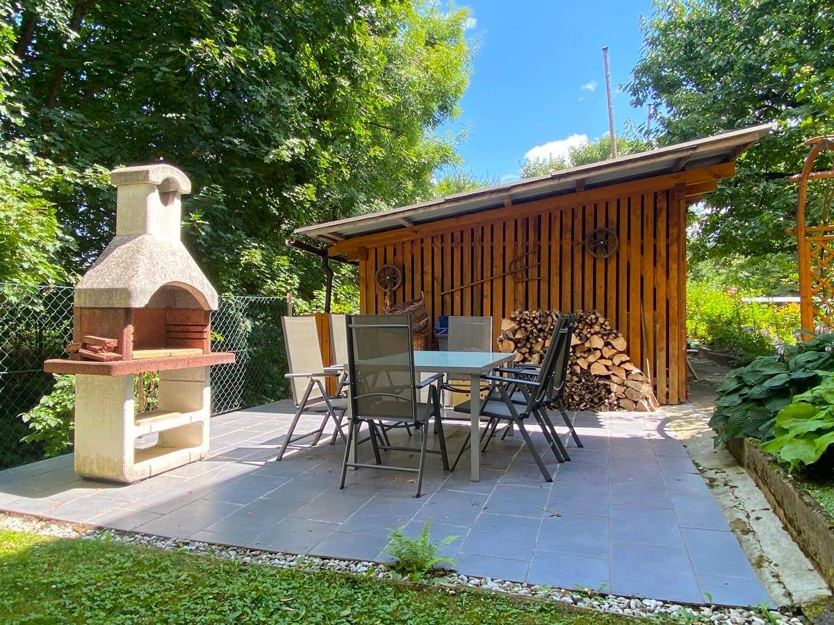 Gemütliche Terrasse mit Steingrill, Sitzgelegenheiten und Holzschuppen im Garten.