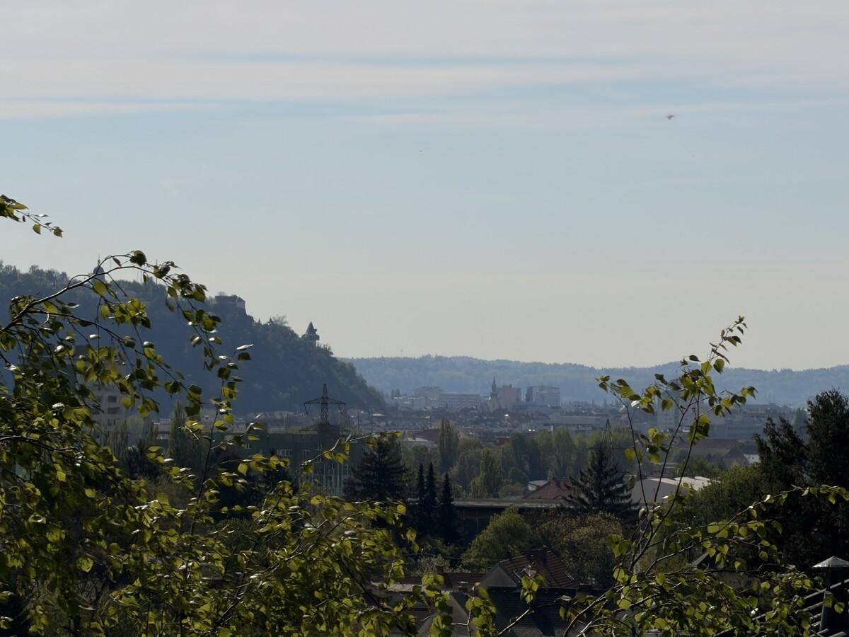 Panoramablick über die Stadt und die umliegende Hügellandschaft unter blauem Himmel.