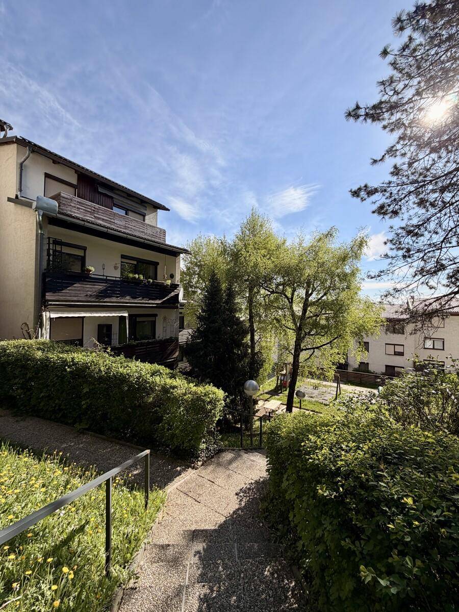 Außenansicht des Gebäudes mit gepflegtem Garten, Wegen und hohen Bäumen.