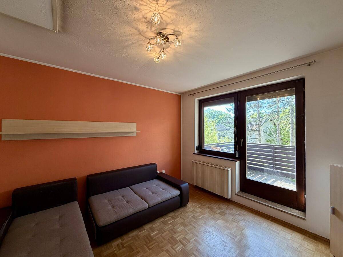 Helles Wohnzimmer mit Parkettboden, orangefarbener Wand und Zugang zum Balkon.
