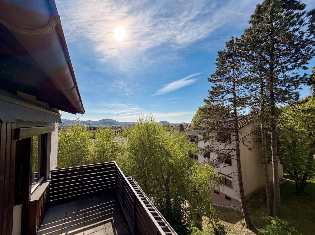 Sonniger Balkon mit Holzzaun und weitem Blick über die grüne Landschaft.