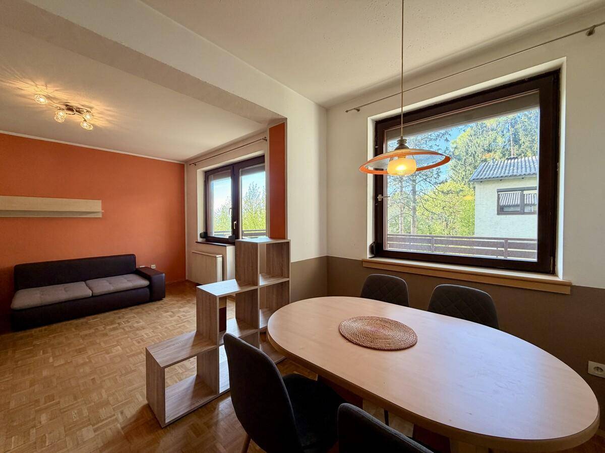Heller Wohn- und Essbereich mit Parkettboden, orangefarbener Akzentwand und großem Fenster.