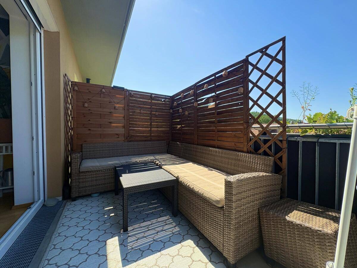 Sonniger Balkon mit bequemen Rattanmöbeln und hölzernen Sichtschutzelementen.