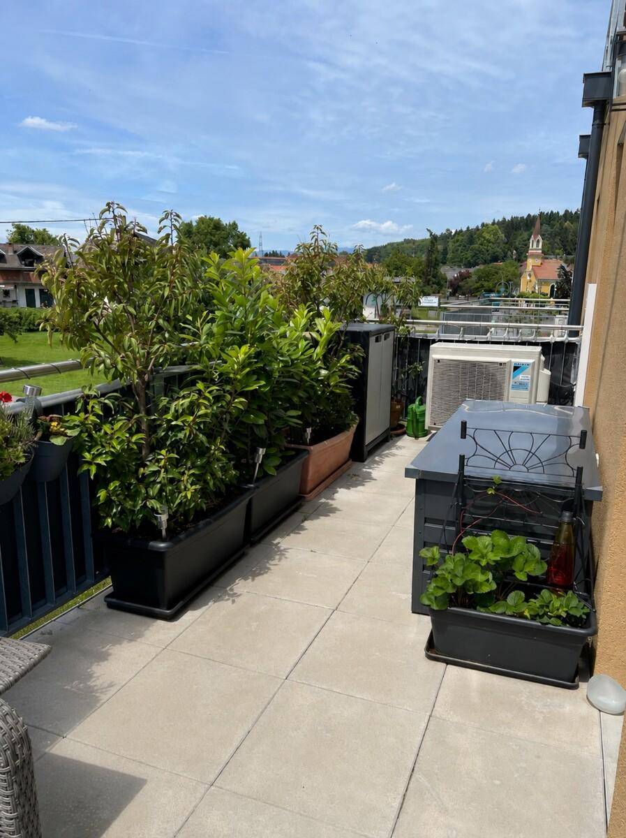 Großer Balkon mit vielen Pflanzen, Außeneinheit der Klimaanlage und Fernblick.