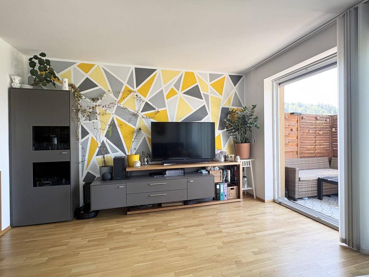 Helles Wohnzimmer mit geometrischer Akzentwand, Mediencenter und Zugang zur Terrasse.
