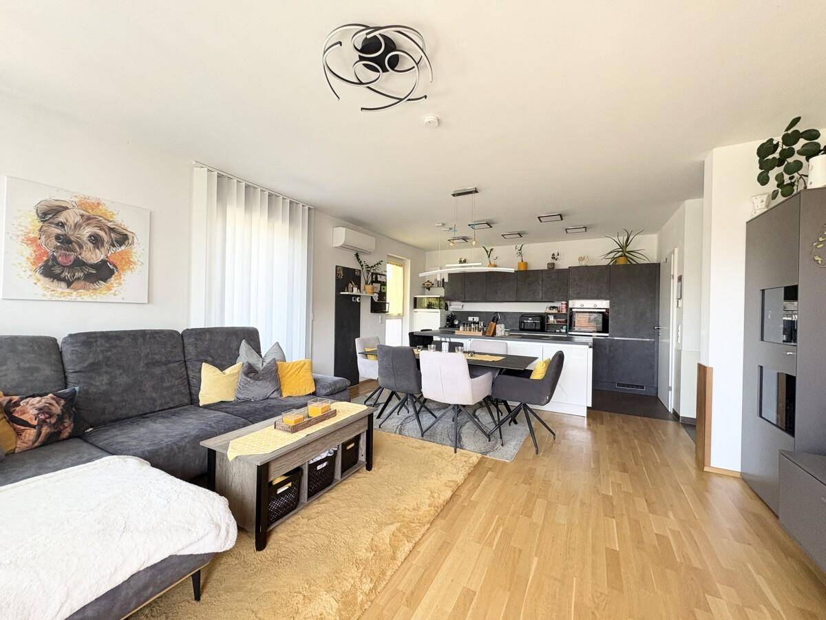 Geräumiger offener Wohnbereich mit Sofa, Essbereich und moderner Küche im Hintergrund.