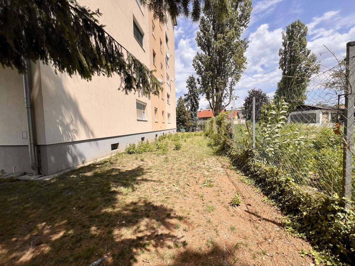 Seitlicher Gartenbereich mit Rasen und Zaun, angrenzend an das Mehrfamilienhaus.