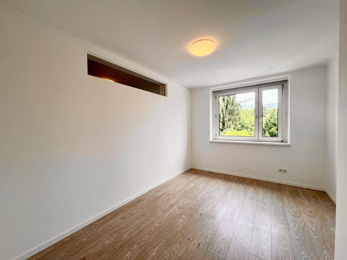 Helles Zimmer mit Laminatboden, hohem Fenster und Blick ins Grüne, geeignet als Schlafzimmer.