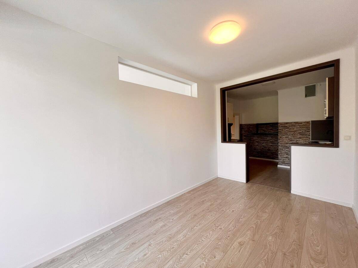 Heller Wohnbereich mit Laminatboden und Durchgang zu einer modern gestalteten Küche.
