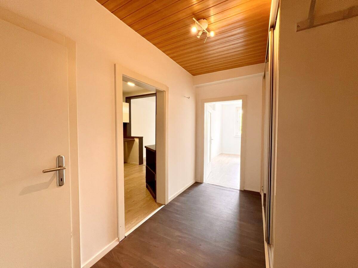 Flur mit Holzpaneeldecke, dunklem Laminatboden und Zugang zu verschiedenen Zimmern.