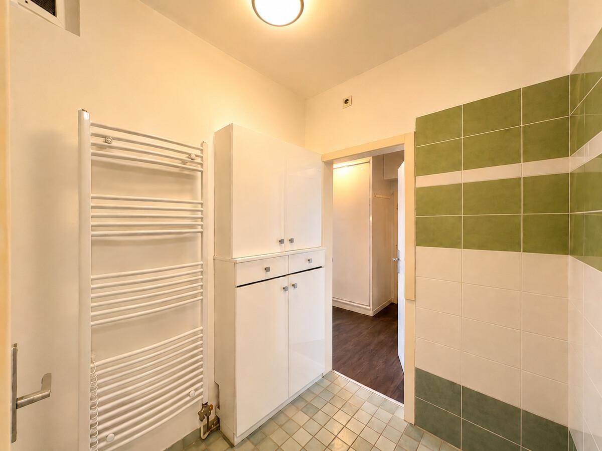 Badezimmer mit Heizkörper, Stauraum und gefliesten Wänden in Grün- und Beigetönen.