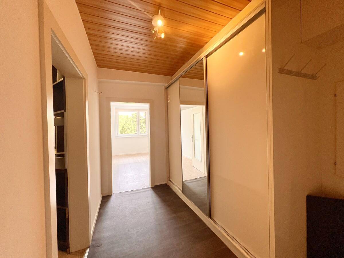 Flur mit Holzpaneeldecke, dunklem Laminatboden und Spiegelschränken, führt zu weiteren Räumen.