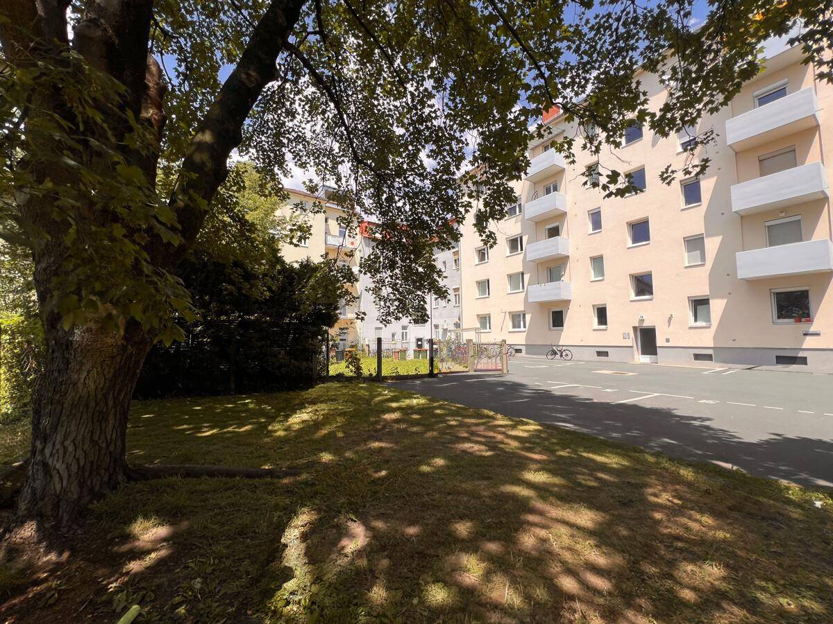 Außenansicht eines Mehrfamilienhauses mit Grünfläche und Bäumen im Vordergrund.