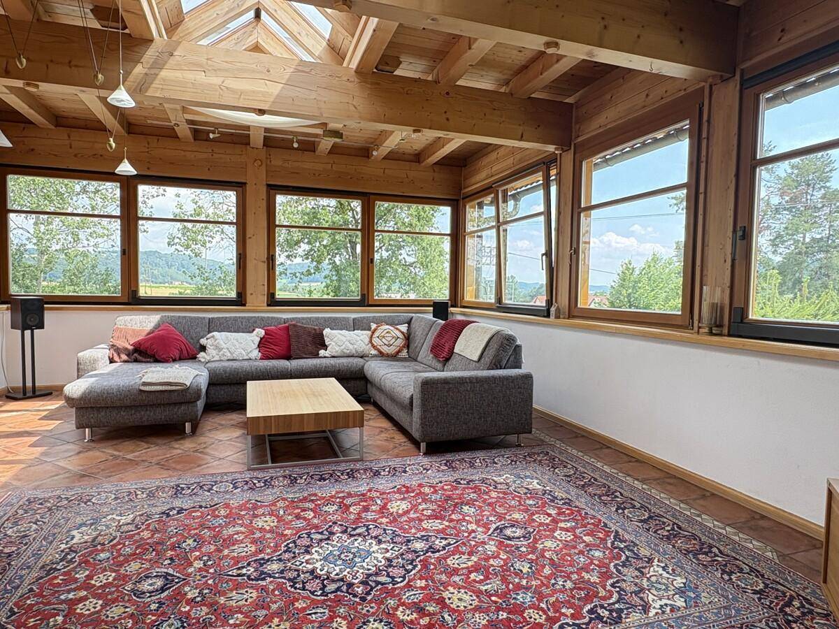 Helles Wohnzimmer im Wintergarten-Stil mit Holzbalkendecke und weitem Ausblick.