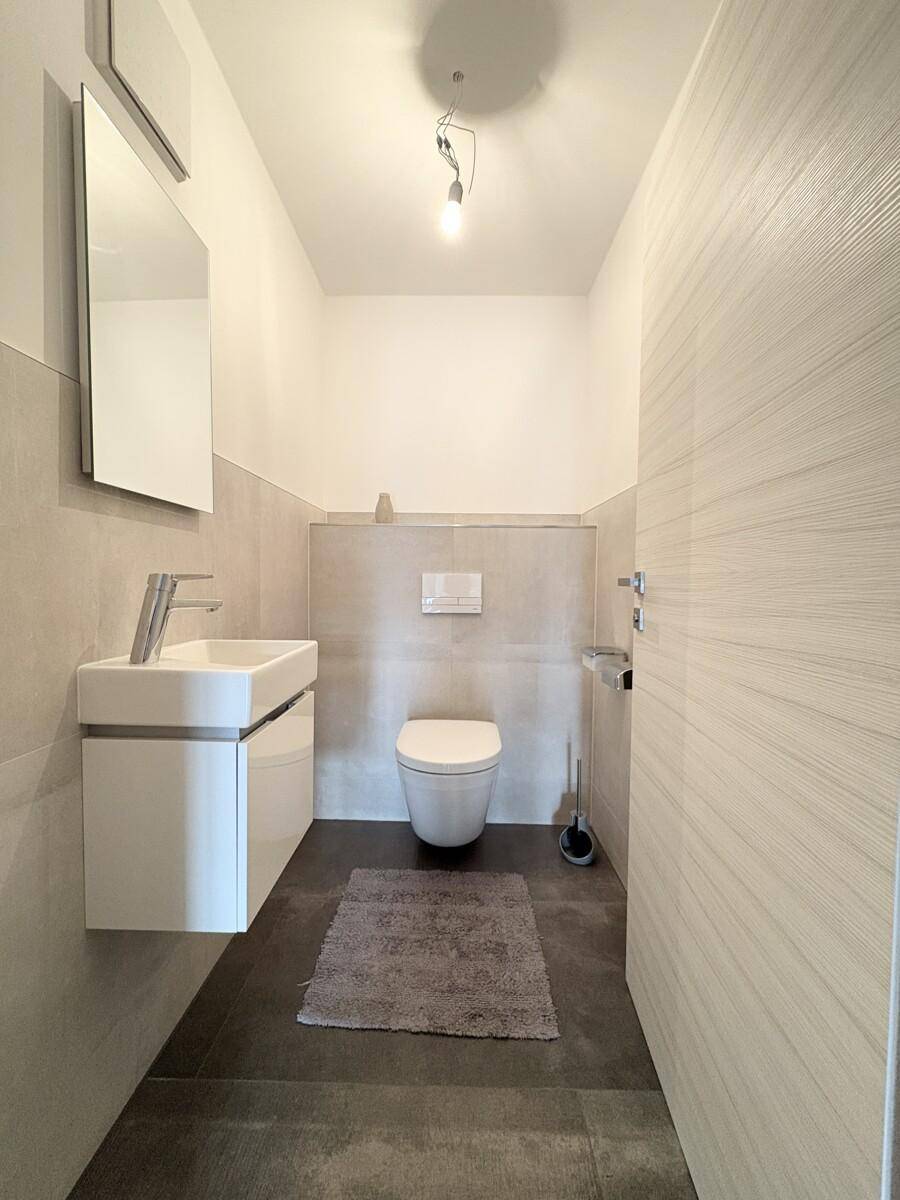 Modernes Gäste-WC mit wandhängendem WC und kleinem Waschbecken, in neutralen Farben gehalten.
