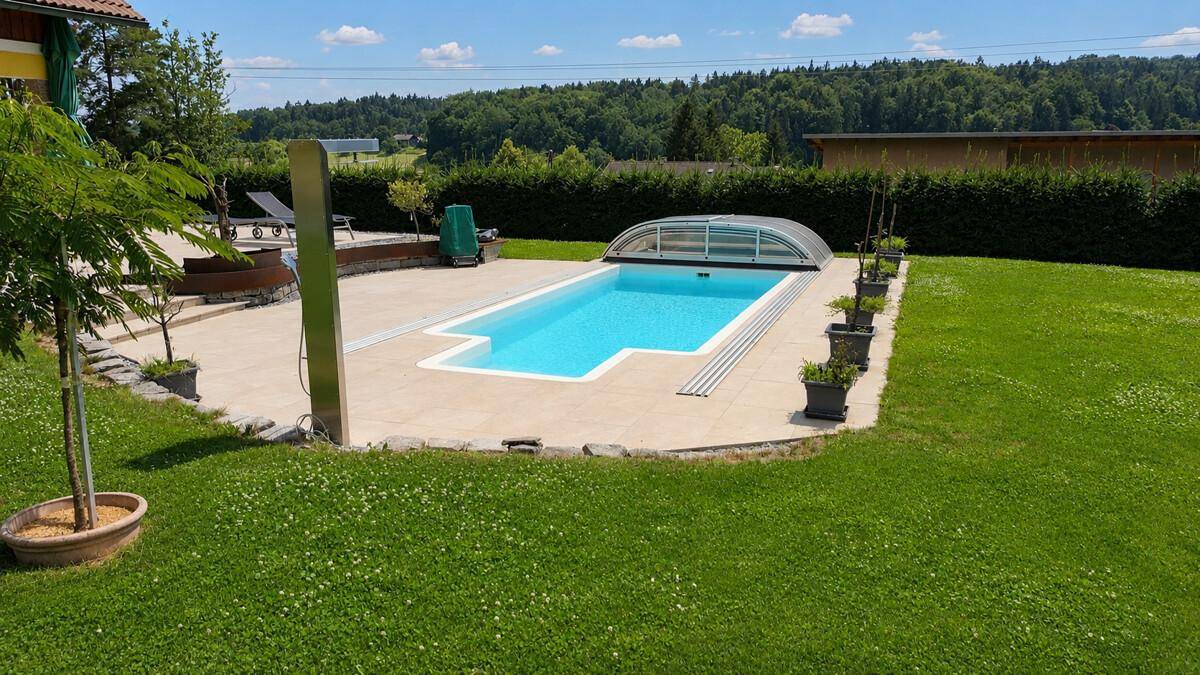 Gepflegter Swimmingpool mit Abdeckung und angrenzender Liegefläche im grünen Garten.