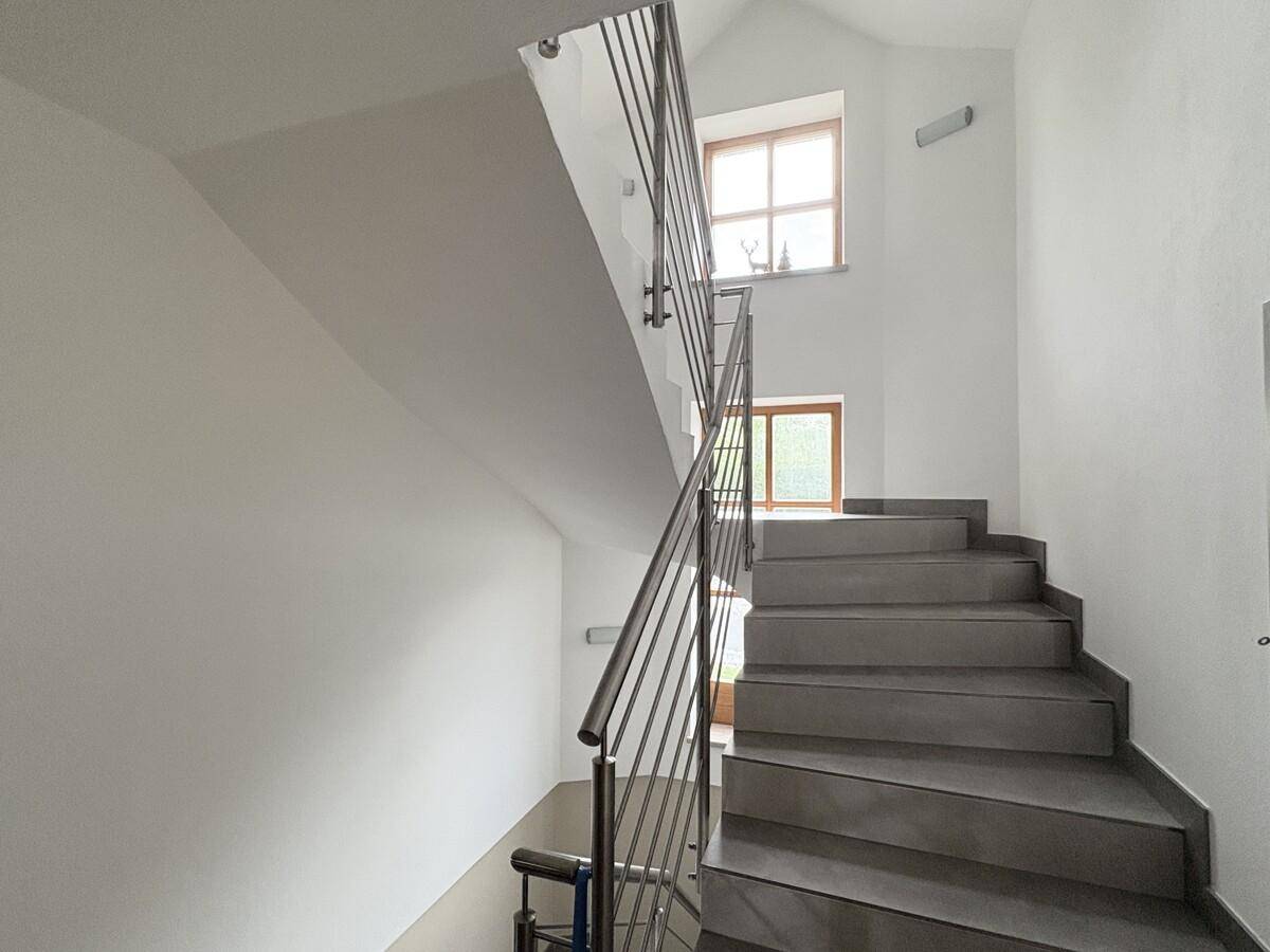 Modernes Treppenhaus mit Edelstahlgeländer und großen Fenstern für viel Licht.