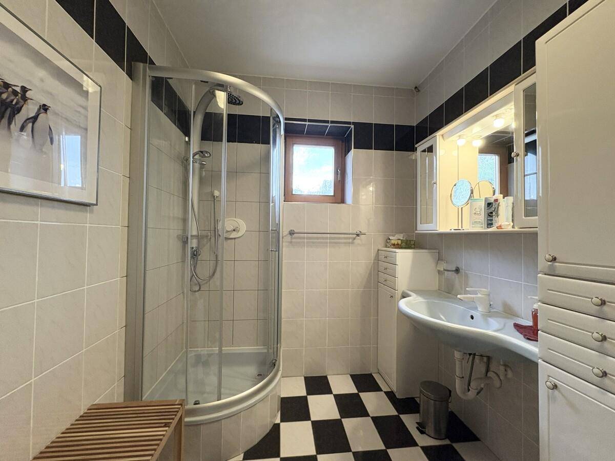 Badezimmer mit Duschkabine, Waschbecken und Fenster, hell gefliest.