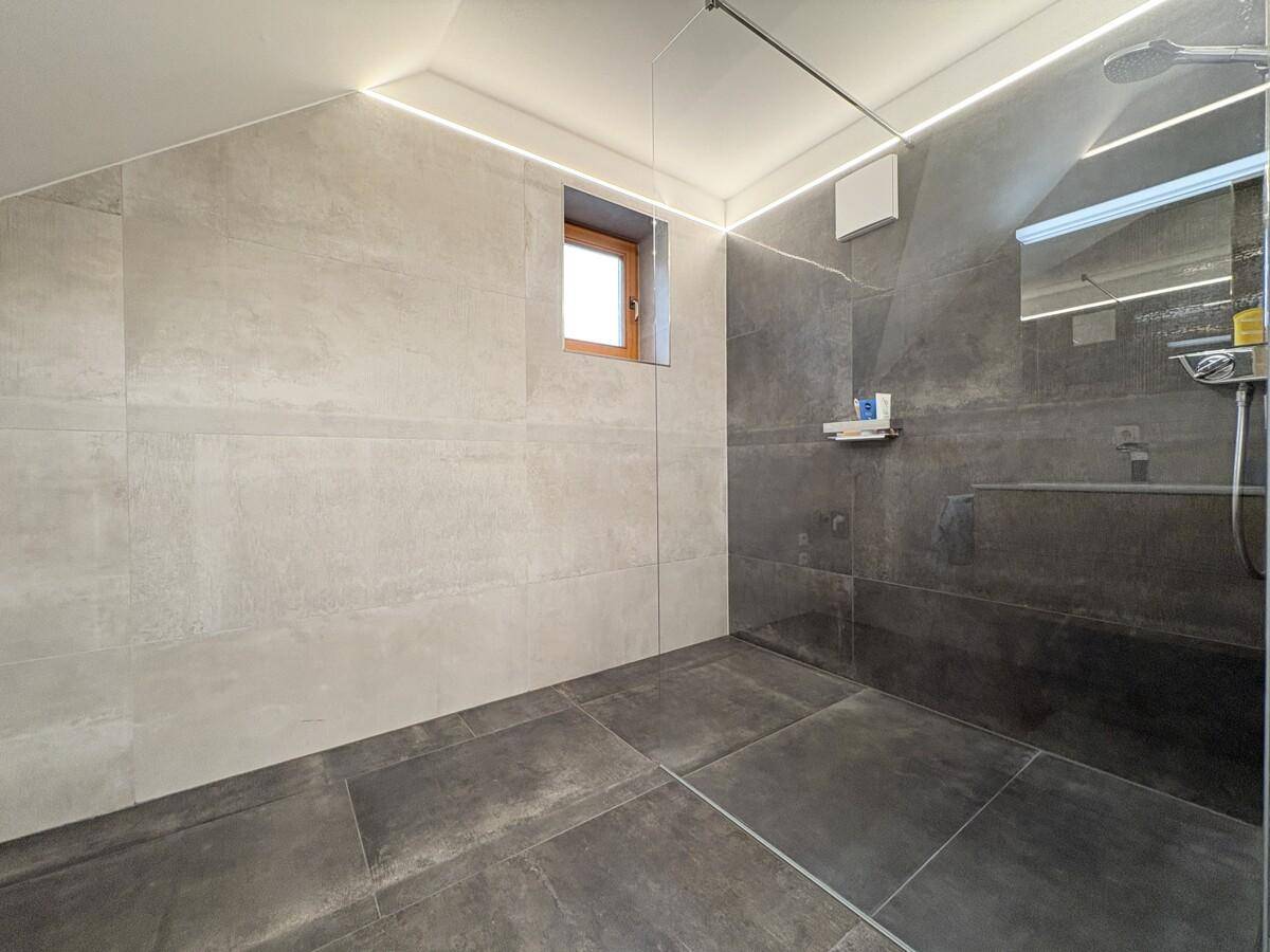 Geräumige, ebenerdige Dusche mit Glasabtrennung und Fenster in einem modernen Badezimmer.