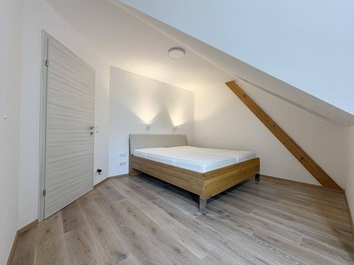 Schlafzimmer im Dachgeschoss mit Holzbett, Holzboden und schräger Decke.