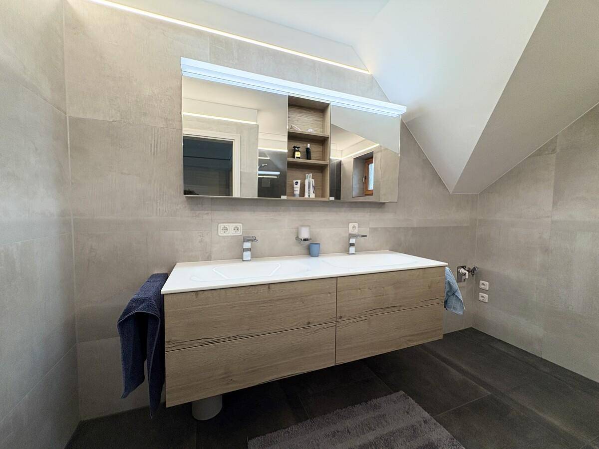 Modernes Badezimmer mit Doppelwaschbecken, großem Spiegelschrank und indirekter Beleuchtung.