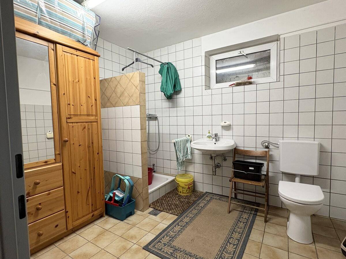 Einfaches Badezimmer im Keller mit Dusche, WC und Fenster, funktional eingerichtet.