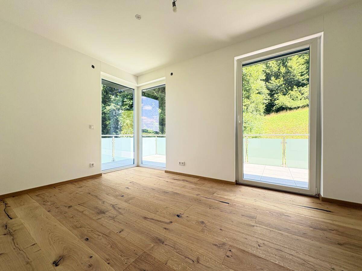 Schlafzimmer mit Holzboden und großen Fenstern, die viel Tageslicht hereinlassen.