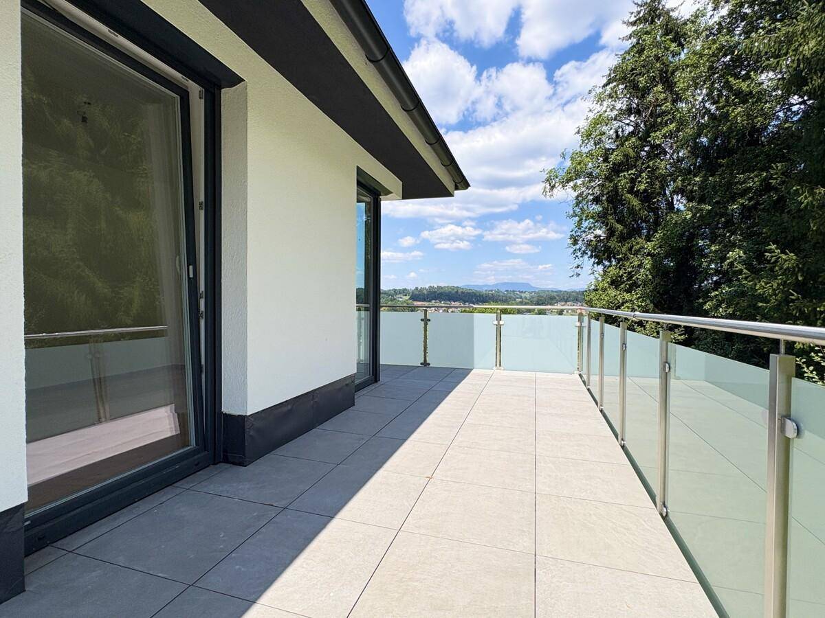 Langer Balkon mit Glasgeländer und Fliesenboden, bietet einen weiten Ausblick.