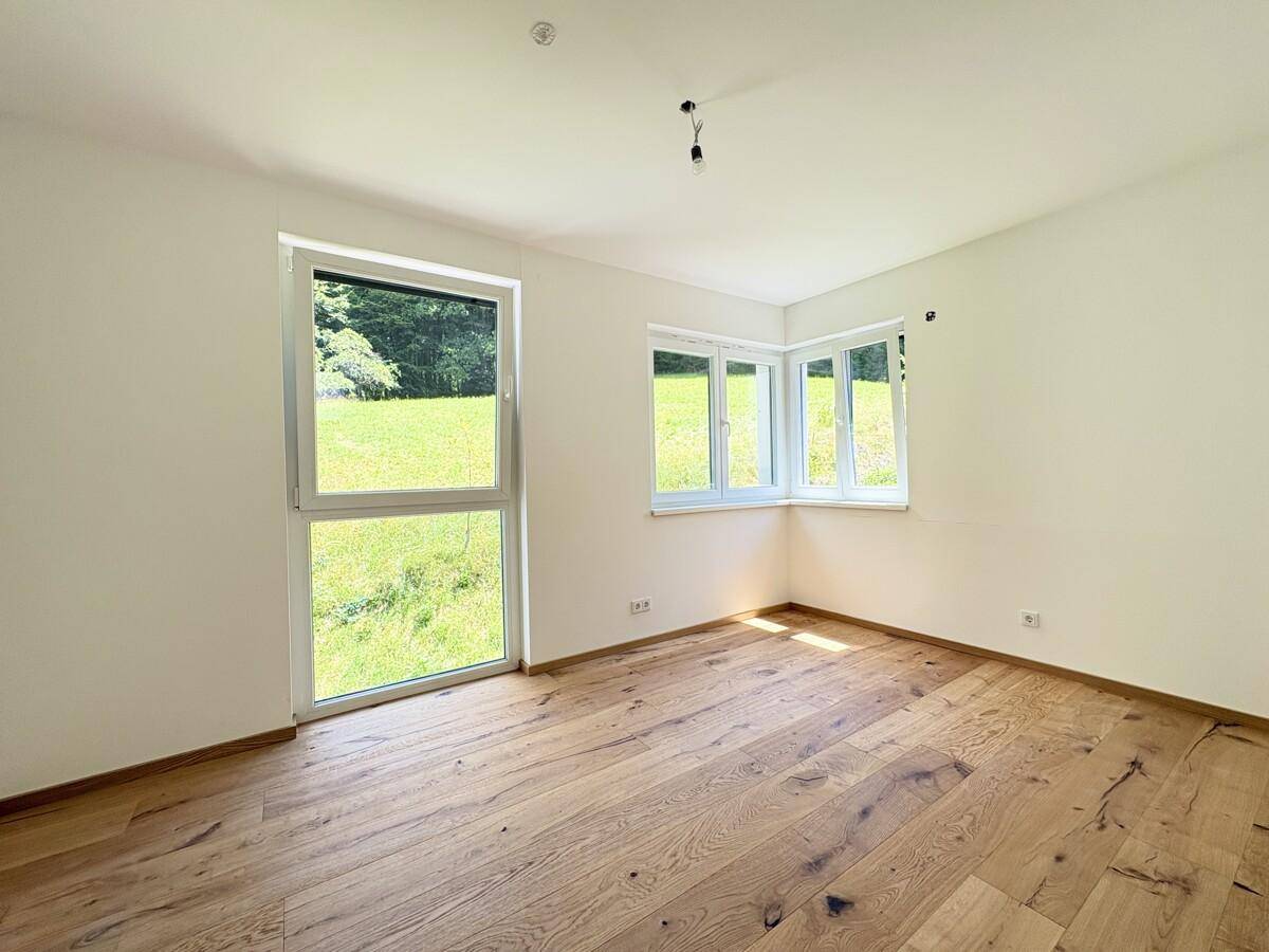 Helles Zimmer mit Holzboden und mehreren Fenstern, die viel Licht spenden.