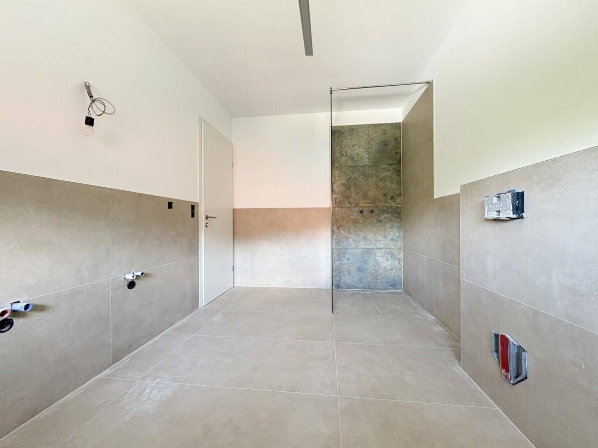 Modernes Badezimmer im Rohbau mit großen Fliesen und vorbereiteten Anschlüssen.