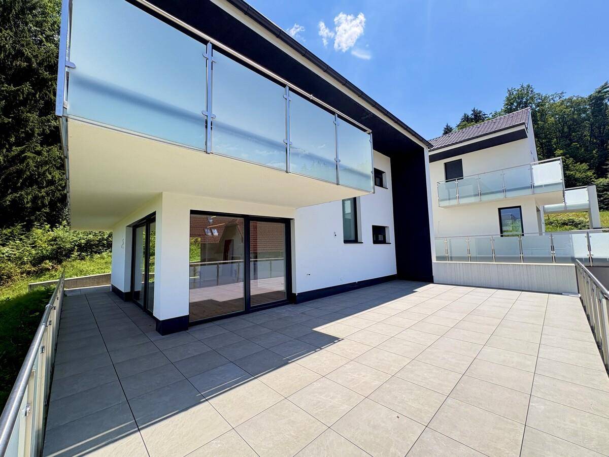 Große, geflieste Terrasse mit Glasgeländer und Zugang zum Innenbereich.