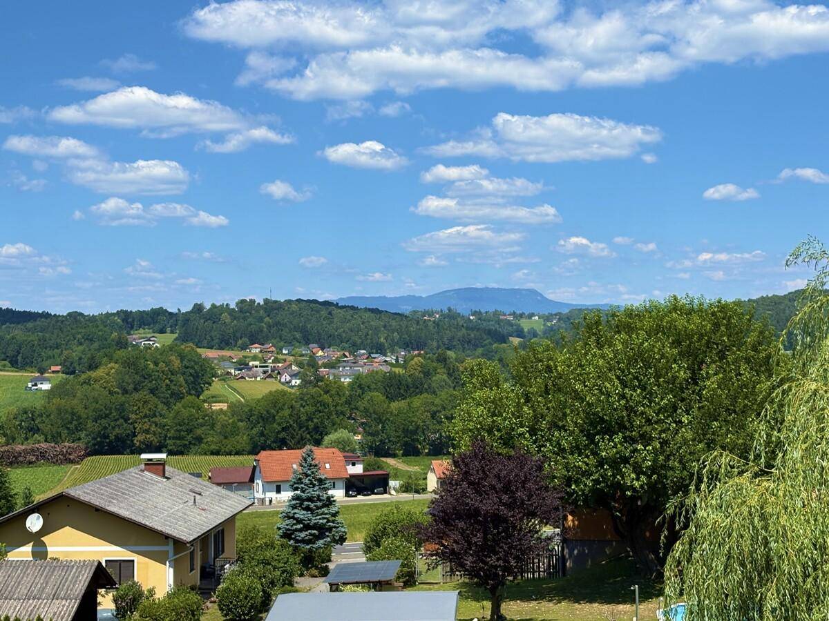 Malerischer Ausblick auf eine ländliche Siedlung mit grünen Hügeln und Bergen im Hintergrund.