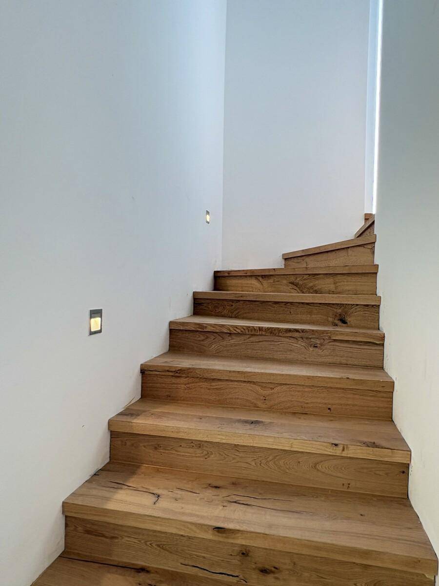 Moderne Holztreppe mit integrierter Beleuchtung und weiß gestrichenen Wänden.