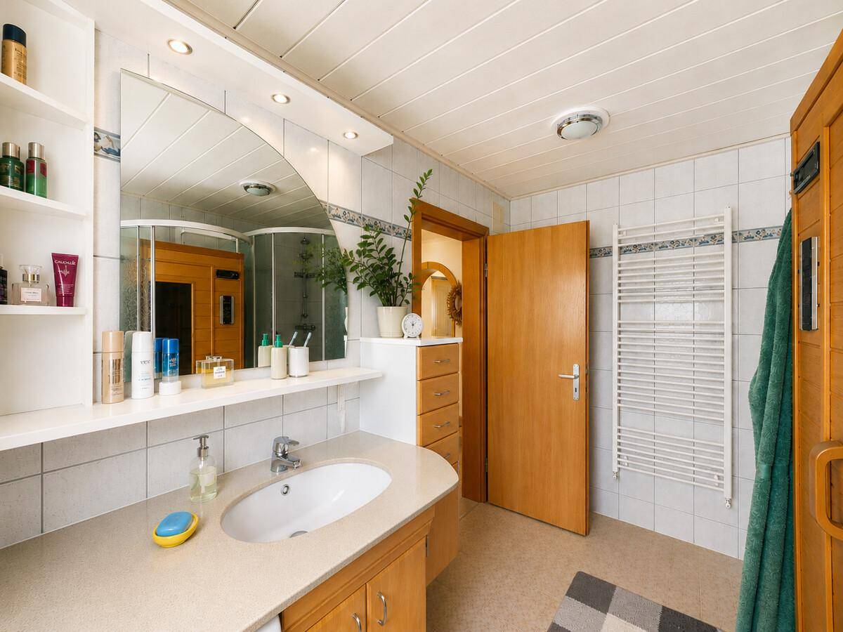 Badezimmer mit Einzelwaschbecken, Spiegelschrank und Zugang zur Sauna.