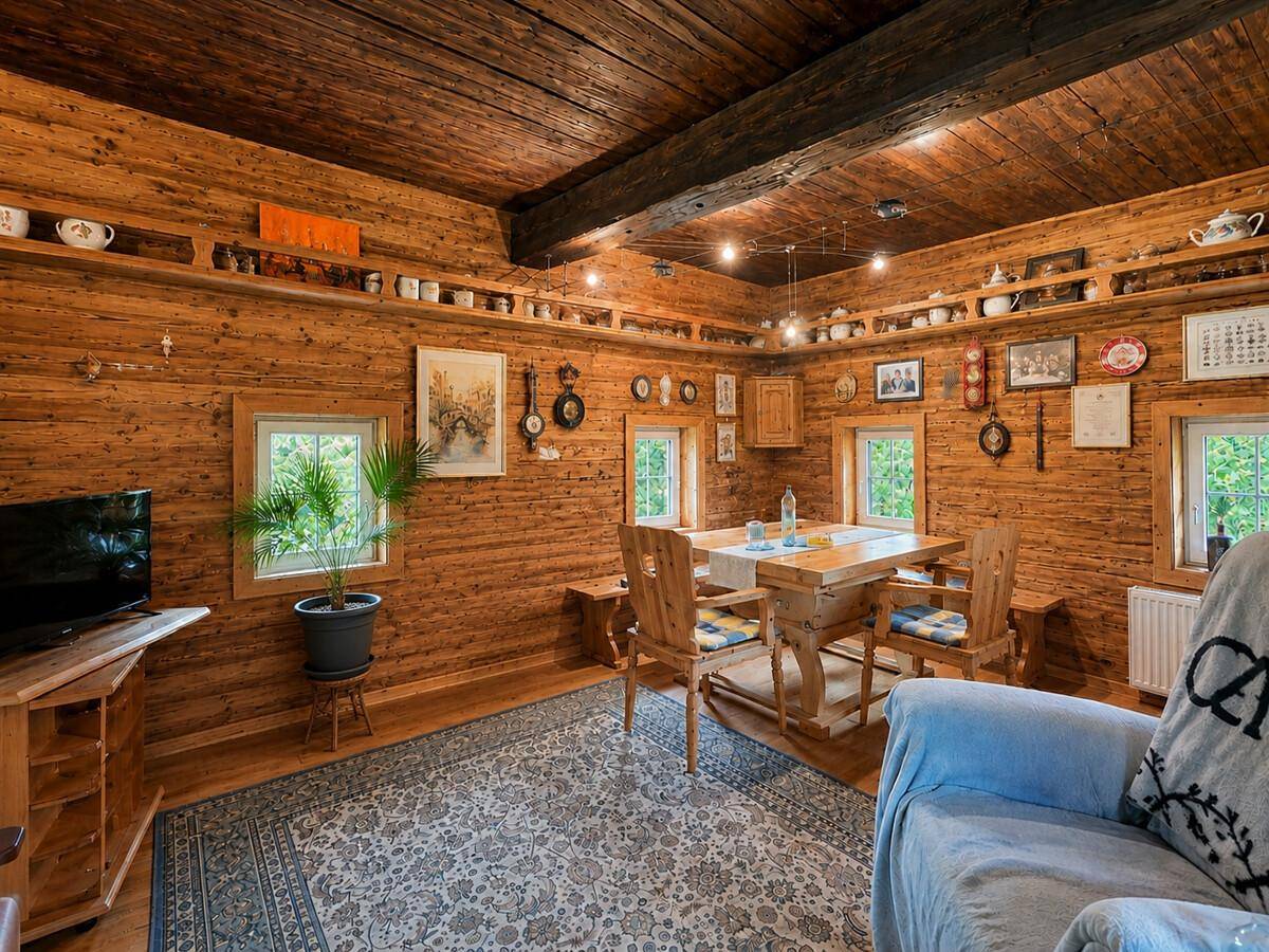 Rustikaler Wohnraum mit holzvertäfelten Wänden, Holzbalken und einem Esstisch.