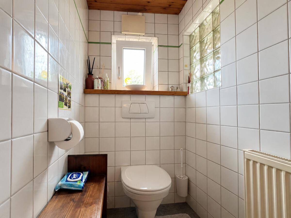 Kleines Gäste-WC mit weißen Fliesen, Fenster und wandmontierter Toilette.