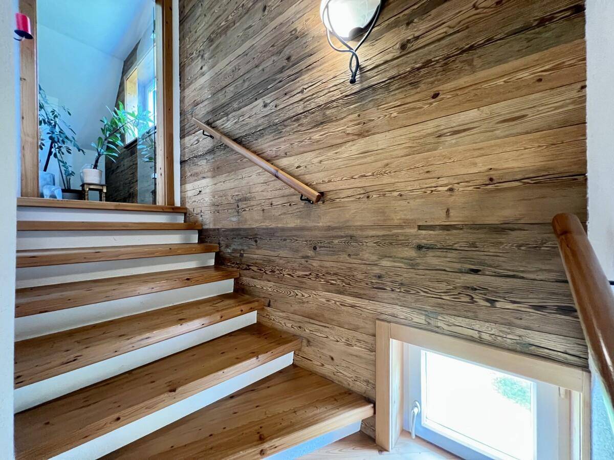 Holztreppe mit rustikalen Holzpaneelen an der Wand, die zu den oberen Etagen führt.